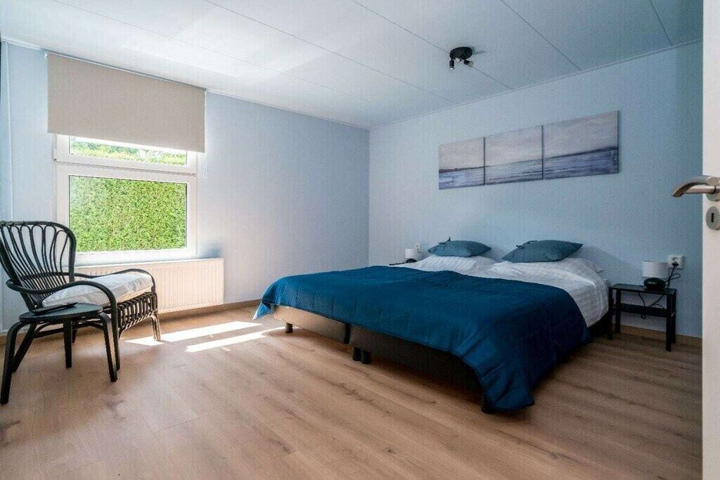 A bedroom with a bed, a chair, a window, and a painting on the wall.