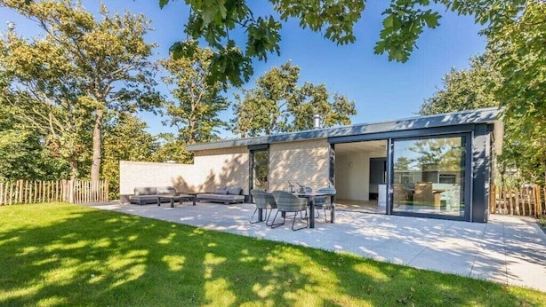 Ein modernes Haus mit Terrasse, Sitzgelegenheiten im Freien und einer Glastür zum Innenbereich.