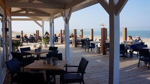 Ein Essbereich im Freien mit Tischen und Stühlen, mit Blick auf einen Strand.