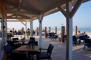 An outdoor dining area with tables and chairs, overlooking a beach. - Holiday home in Renesse with swimming pool (Renesse)