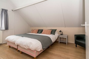 A bedroom with a sloped ceiling, a bed with a striped headboard, a bedside table with a lamp, and a chair. - Holiday home in Renesse with swimming pool (Renesse)