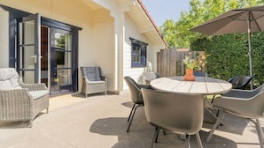 Eine Terrasse im Freien mit einem runden Tisch und Stühlen, einer Rattan-Couch und einem Blumentopf.