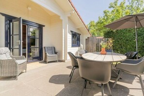An outdoor patio with a round table and chairs, a wicker sofa, and a potted plant. - Holiday home in Renesse with swimming pool (Renesse)