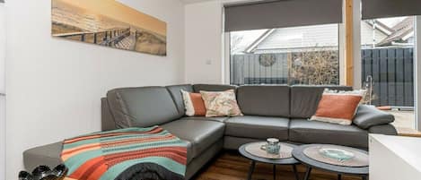 A modern living room with a grey sectional sofa, a colorful woven blanket, a wooden side table, and two small round tables.