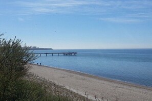 A beach with a pier extending into calm waters, a clear sky, and sparse vegetation. - Holiday home with 1 bedroom (Ostseebad Rerik)