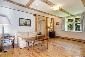 A room with a wooden floor, a white sofa, a wooden coffee table, a lamp, and a painting on the wall. - Green Cottage by the Swan Pond (Lassan)