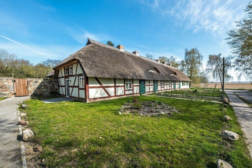 Een traditioneel vakwerkhuis met rieten dak, omringd door een verzorgd gazon en een stenen muur.