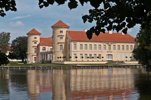 A large stately building with a central tower and a symmetrical facade, situated across a body of water. - Bungalow in Priepert with swimming pool (Priepert)