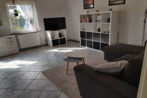 Een woonkamer met een bank, een televisie, een witte boekenkast en een raam met uitzicht.
