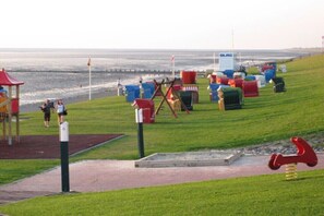 Ein Spielplatz mit Schaukeln, einer Wippe, einem kleinen Spielhäuschen und einem Wasserspielbereich.