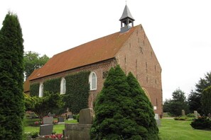 Eine Kirche mit Glockenturm, Efeu bewachsenen Mauern und einem Friedhof im Vordergrund.