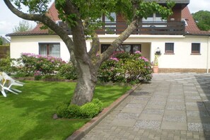 Une maison à deux étages avec une allée pavée, une pelouse et des arbustes en fleurs.