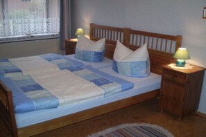 Un lit double avec une couette bleue et blanche, deux tables de chevet avec des lampes et une fenêtre avec un rideau blanc.