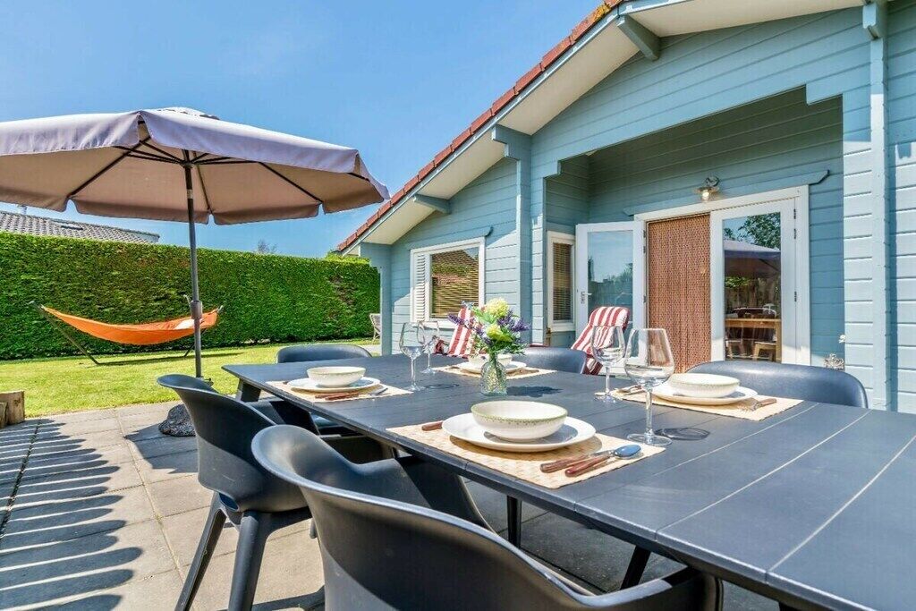 Un espace de restauration en plein air avec une table dressée pour quatre personnes, des chaises, un parasol et un hamac.