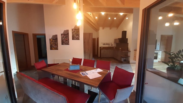 Ein Essbereich mit einem Holztisch und roten Stühlen, eine Küche im Hintergrund und Kunstwerke an den Wänden.