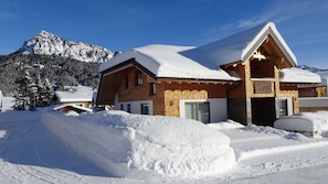 A chalet-style building with a sloped roof, surrounded by snow-covered terrain and mountains in the background.