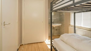 Ein Schlafraum mit Etagenbetten, einer Tür, einem Waschbecken und einem Fenster mit Jalousien.