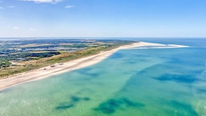 Eine Vogelperspektive auf eine Küstenlandschaft mit einem klaren Strand und ruhigem Wasser.