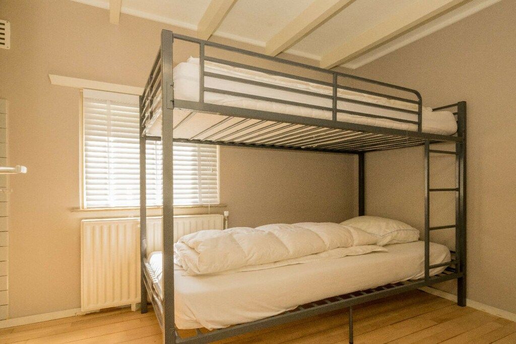 A bunk bed with a white mattress and pillows, a window with blinds, and a radiator.