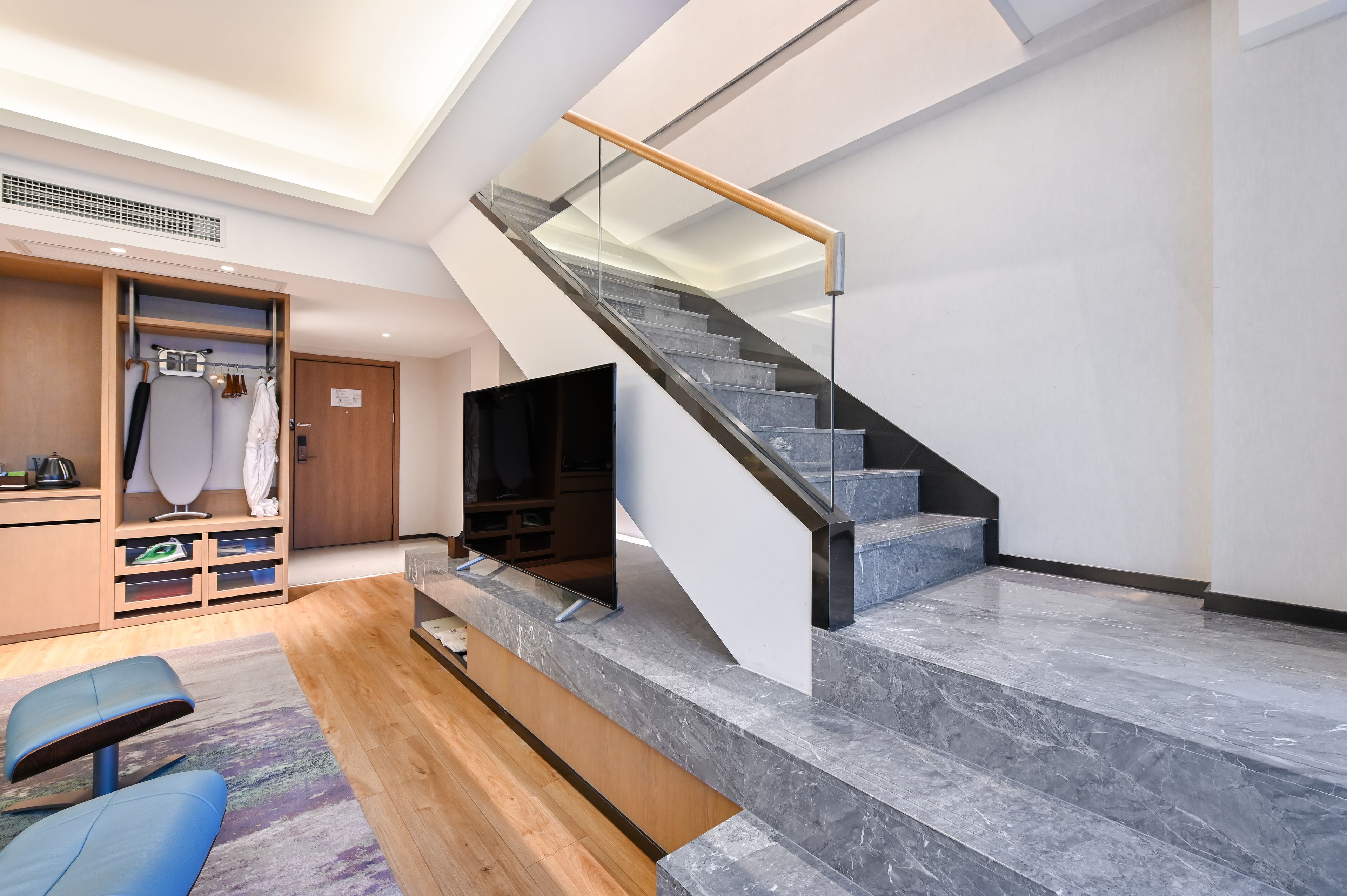 A modern interior with a staircase, a flat-screen TV, and a wooden wardrobe.