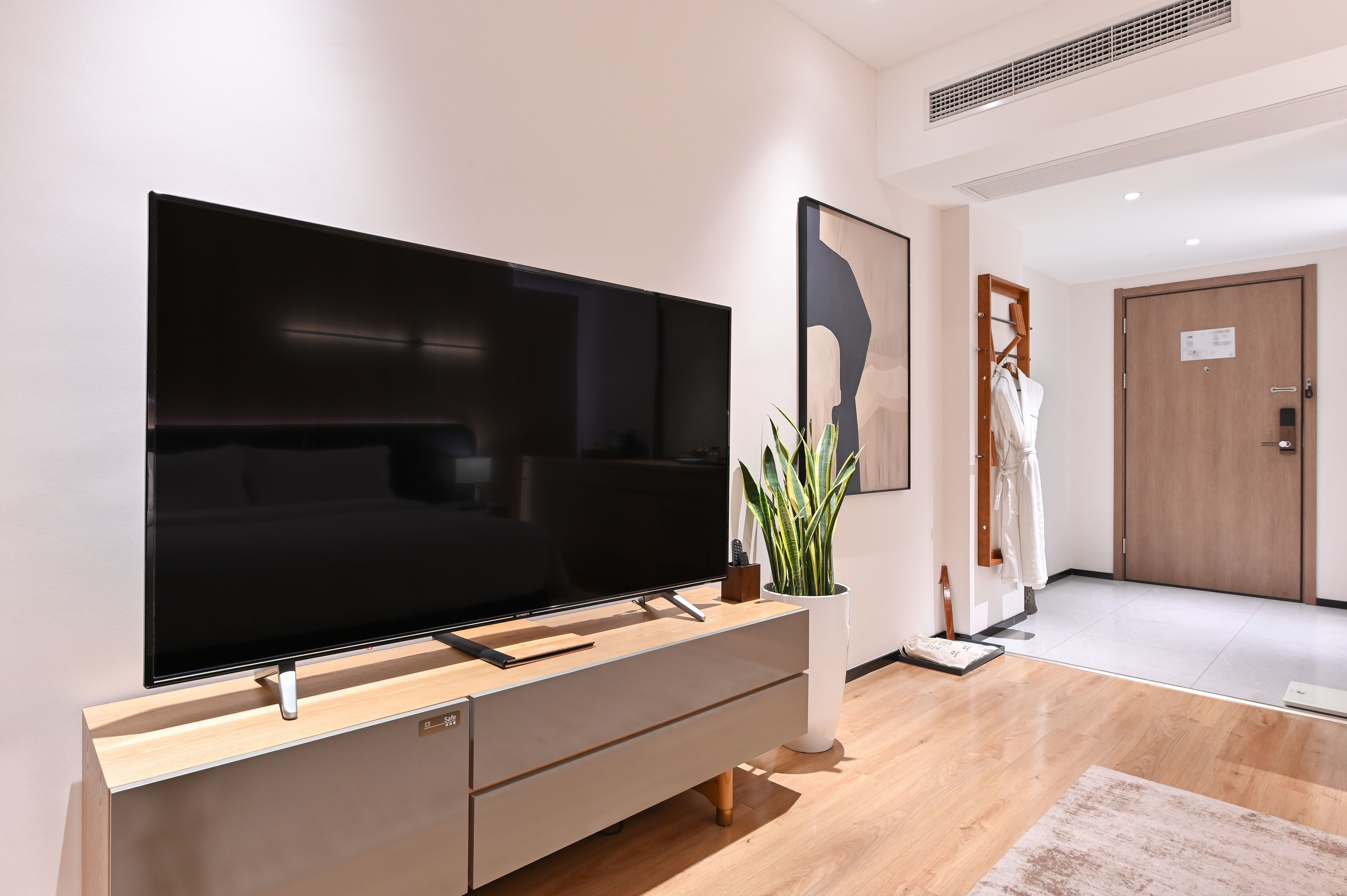 Una sala de estar moderna con un televisor de pantalla plana grande sobre un mueble de madera, una planta en maceta y una puerta con perchero.