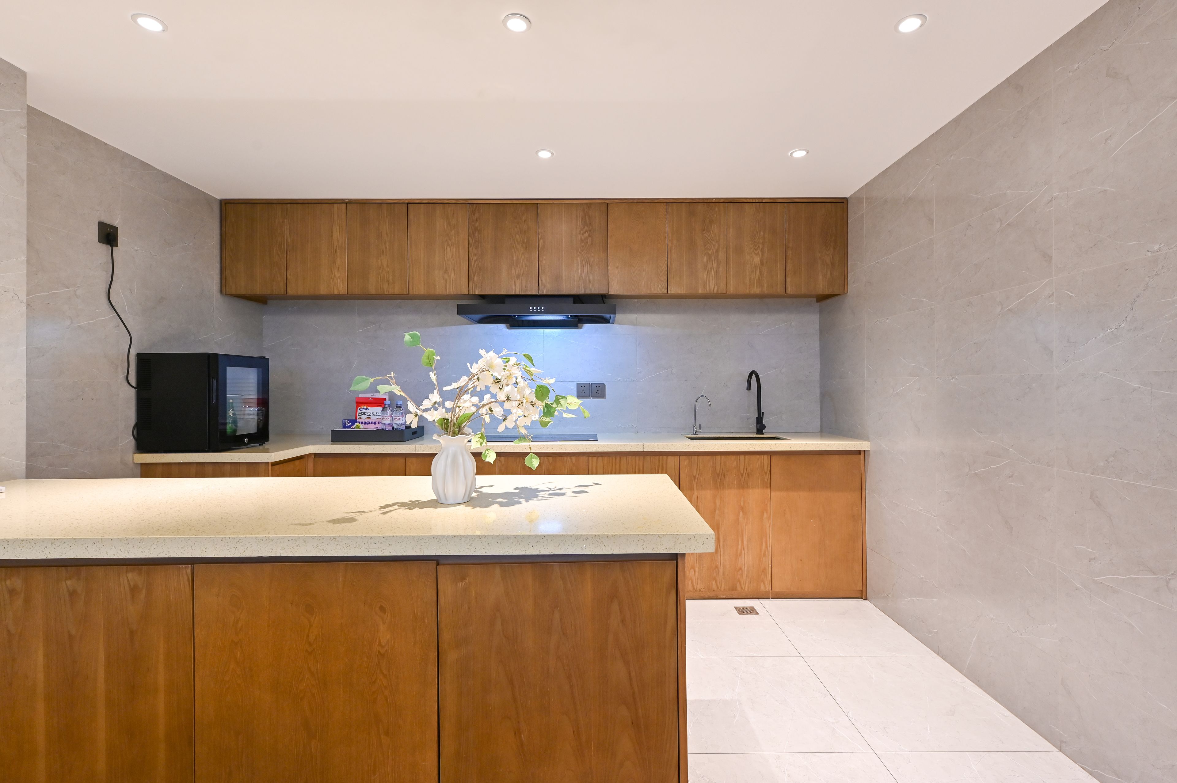 A modern kitchen with wooden cabinets, a built-in microwave, and a vase with flowers on the counter.