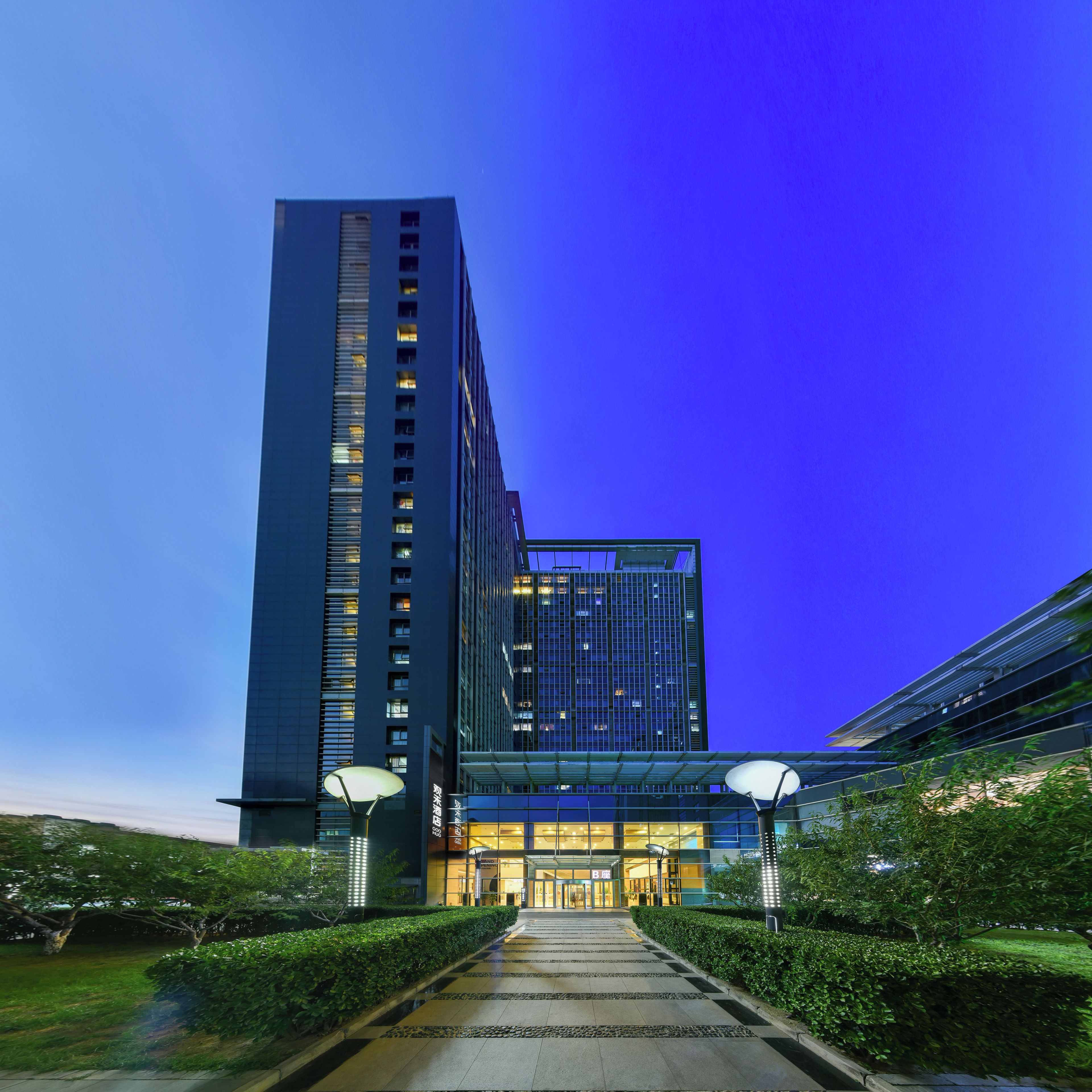 A modern building with a prominent entrance, a glass facade, and a well-maintained garden area.