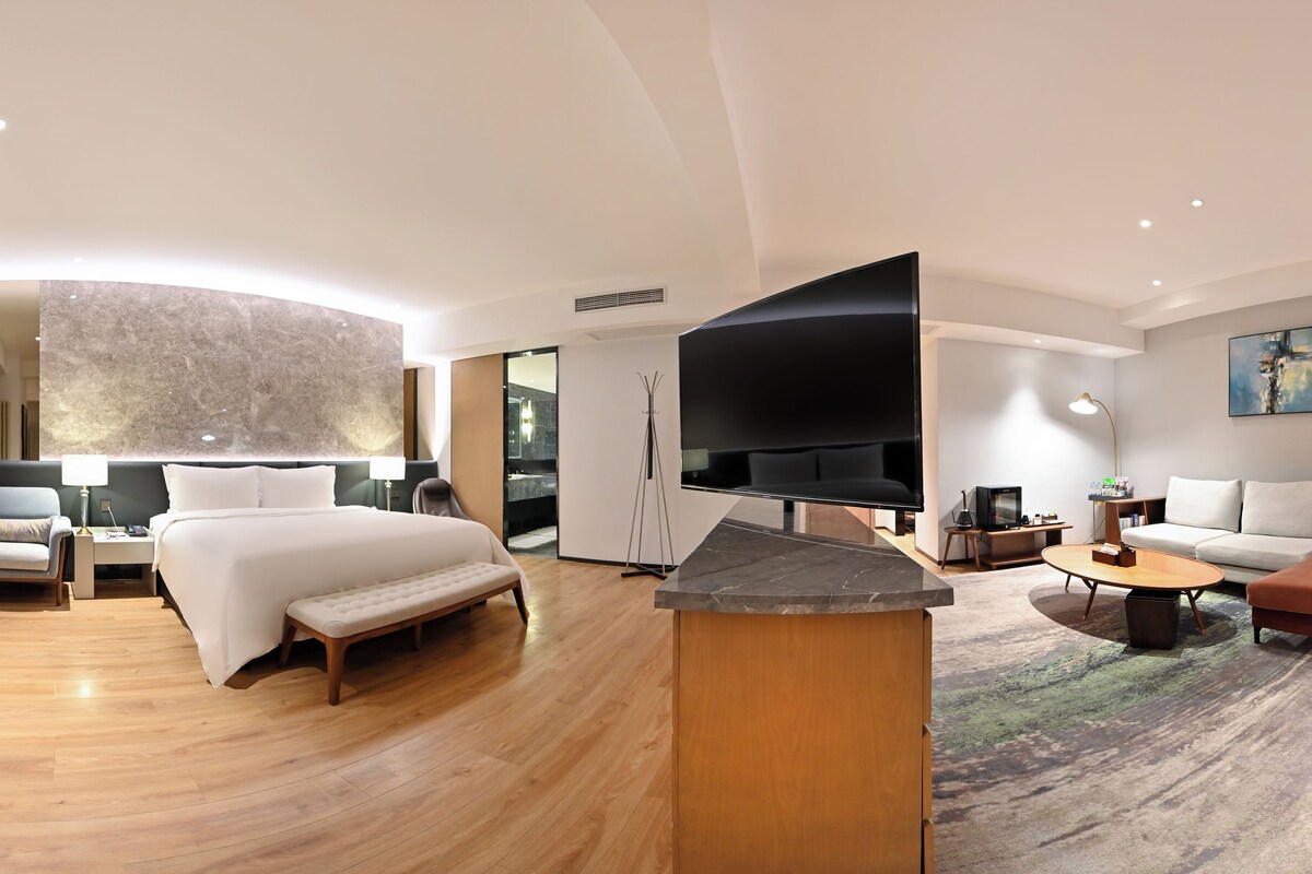 A modern hotel room with a large bed, a flat-screen TV, a sofa, and a coffee table.