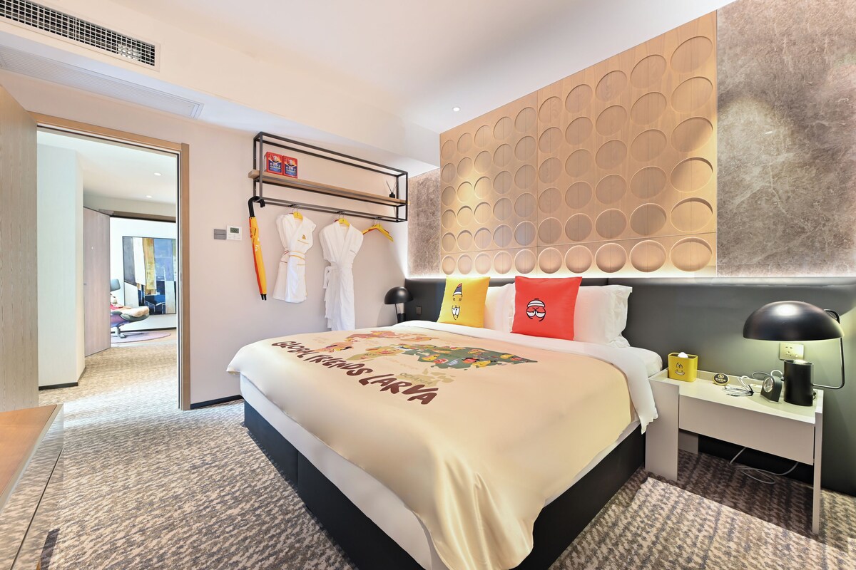 A hotel room with a bed, a desk, a lamp, and a wall with circular patterns.