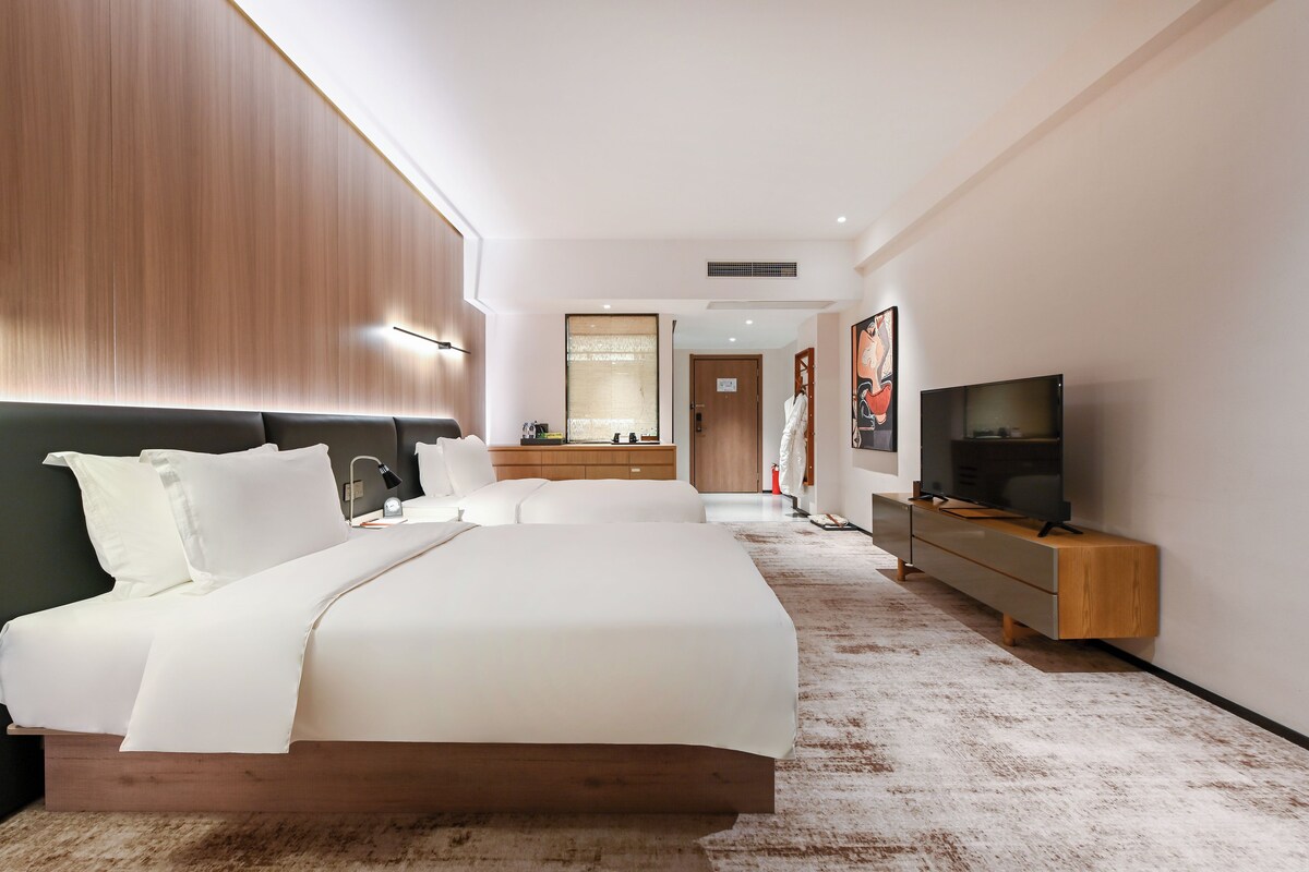 A modern hotel room with a large bed, a TV, a bedside table, and a wardrobe.