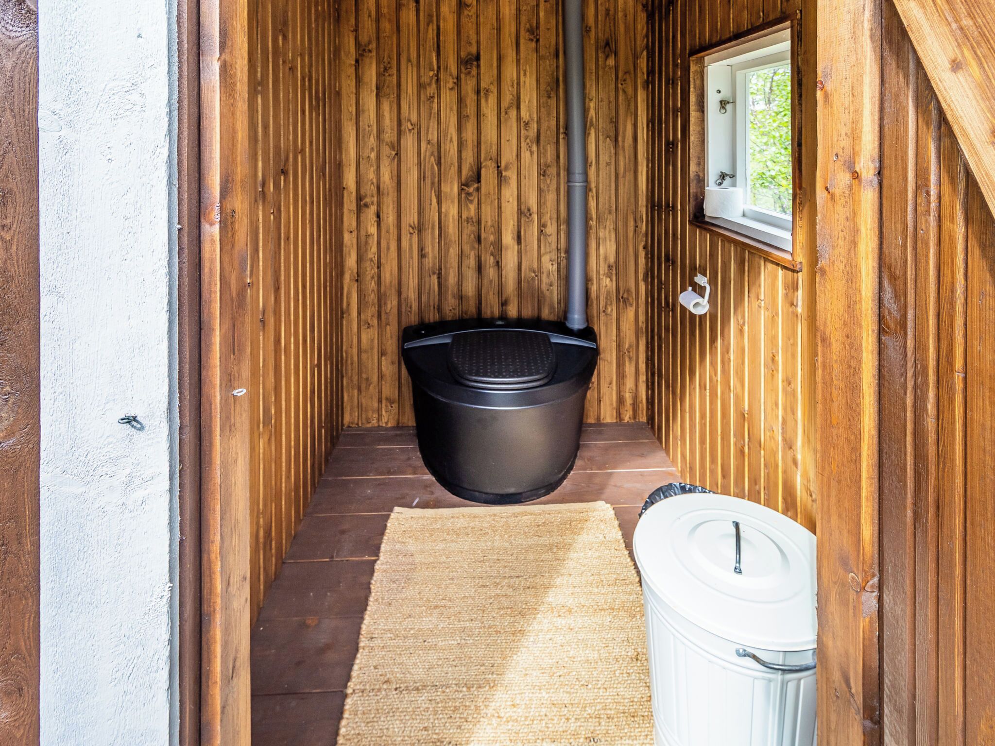 Kapea puinen käytävä, jossa on musta roskakori ja valkoinen roskasanko.