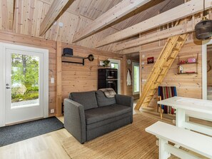 Interior acollidor d'una cabana amb un sofà, una escala de fusta i una taula de dinar.