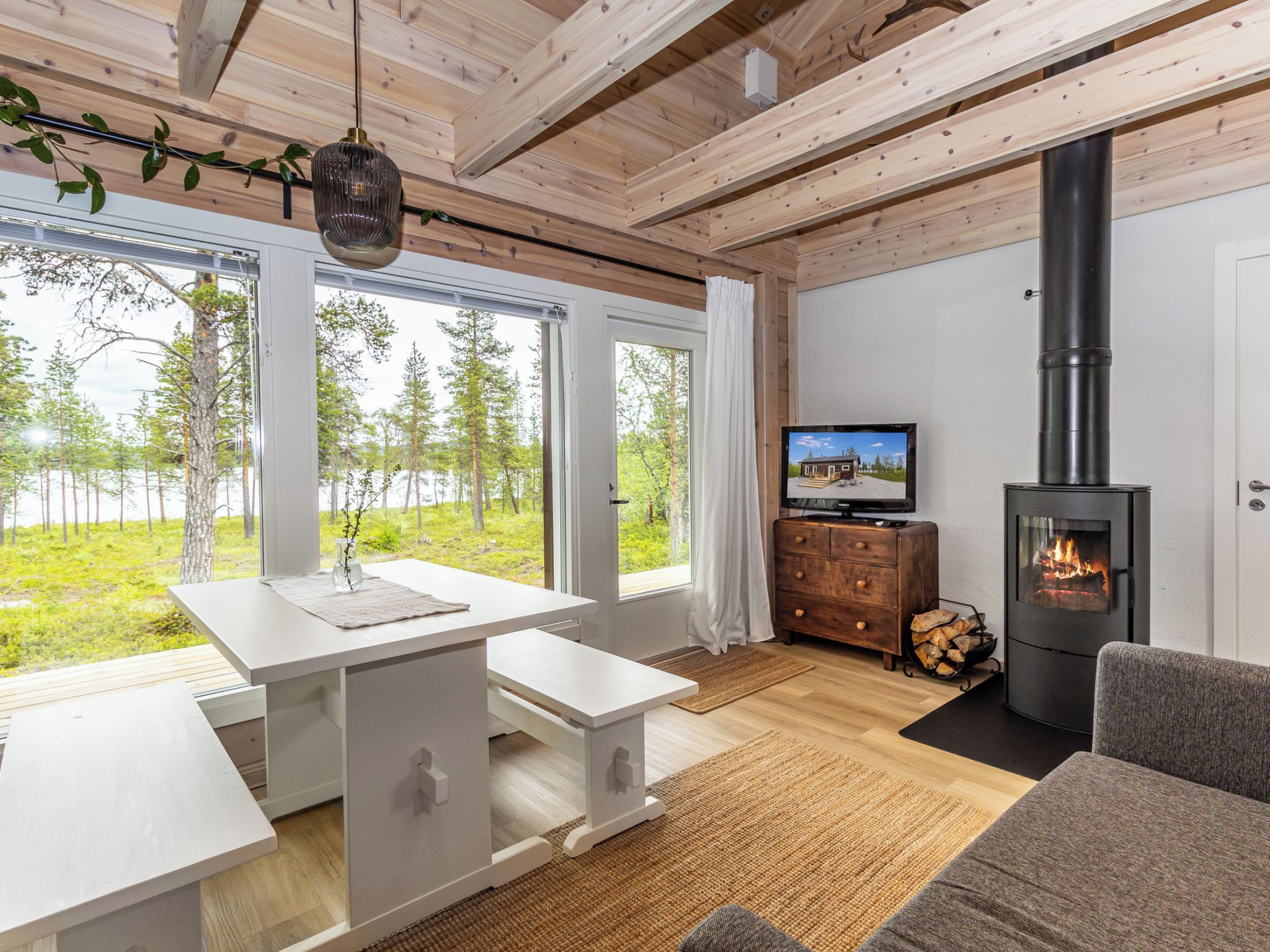 Un intérieur moderne avec un plafond en bois, une cheminée, un téléviseur et une vue sur une forêt.