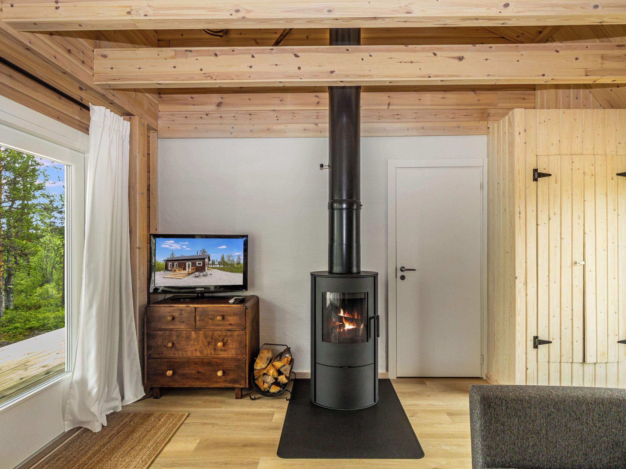 A cozy room with a wood-burning stove, a television, and a view of a house through a window.
