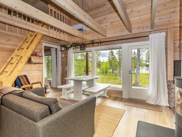 A cozy cabin interior with a loft bed, a dining area with benches, and a fireplace.