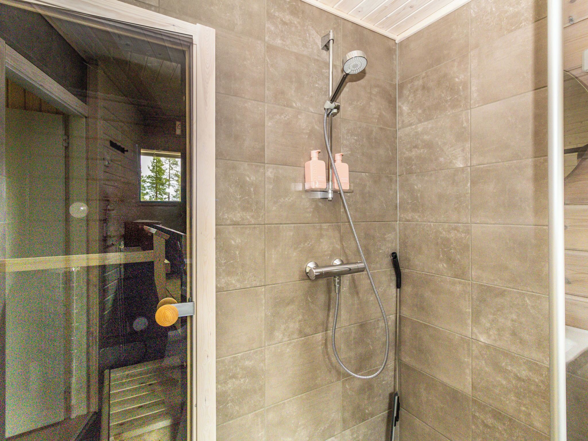 A shower with a handheld showerhead, a wall-mounted faucet, and a handheld shower hose. There are two bottles of shampoo and conditioner on the wall.