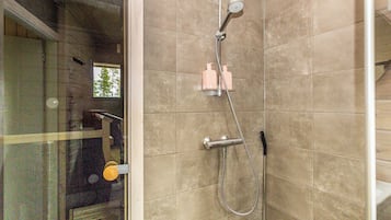 A shower with a handheld showerhead, a wall-mounted faucet, and a handheld shower hose. There are two bottles of shampoo and conditioner on the wall.