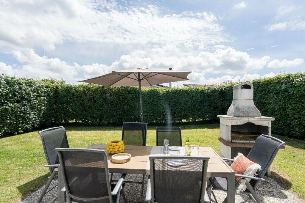 An outdoor patio with a table set for dining, surrounded by chairs, a large umbrella, and a stone fireplace.