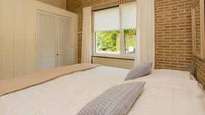 Ein Schlafzimmer mit einem Bett, einem Fenster mit Vorhängen, einer Heizung und einer Ziegelwand.