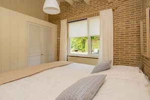 A bedroom with a bed, a window with curtains, a radiator, and a brick wall. - Holiday home in Renesse with swimming pool (Renesse)
