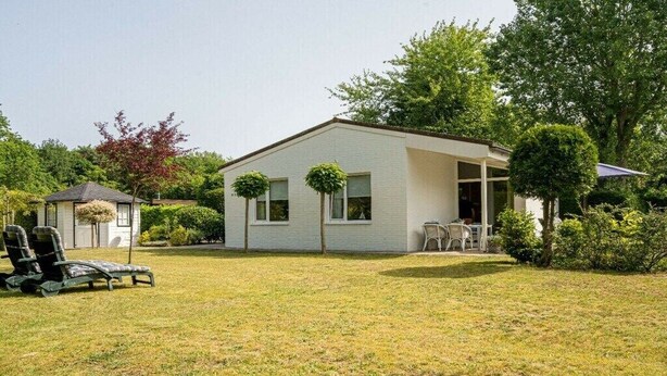 Einbungalow mit überdachter Terrasse, Rasen und kleinem Garten.