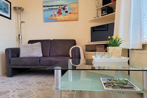 A living room with a sofa, a glass coffee table, a painting on the wall, and a bookshelf. - Holiday apartment with 2 bedrooms (Callantsoog)