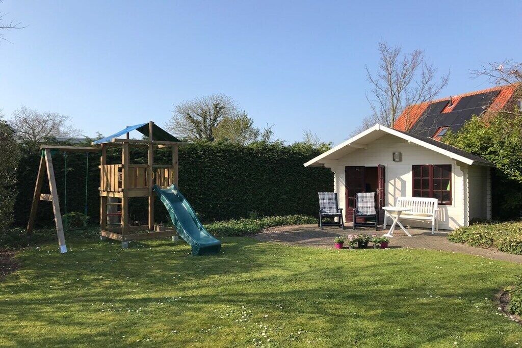 Una propiedad residencial con un parque infantil de madera, una casa blanca de techo rojo y un césped bien cuidado.
