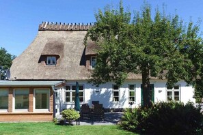 Ein traditionelles Haus mit einem Strohdach, einer Veranda mit Stühlen und einem kleinen Fenster.
