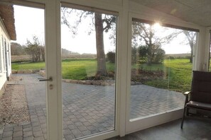 Une pièce dotée d’une porte vitrée donnant sur un patio extérieur, avec un sol en briques et un banc.