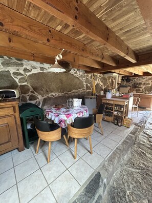 A rustic kitchen with stone walls, wooden beams, a tiled floor, and a table set for dining. - An exceptional sheep farm on the hills above Ercé — the wild and unspoiled Ariège (Ercé)