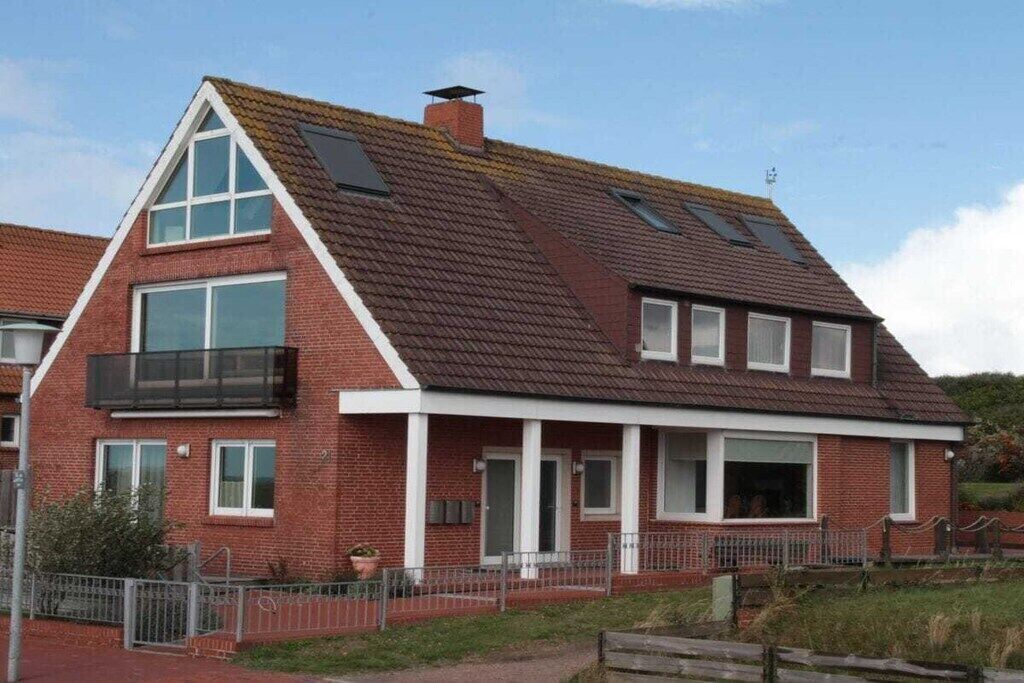 A two-story brick house with a gabled roof, large windows, and a balcony.