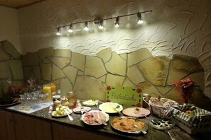 Een ontbijtbuffet met diverse gerechten, een bordje met de tekst 'Frühstück' en een stenen muur met een bladmotief.