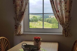 A room with a window overlooking a green landscape, a table with a basket and a vase of flowers. - 5 in the house Traumweide (Oberwiesenthal)