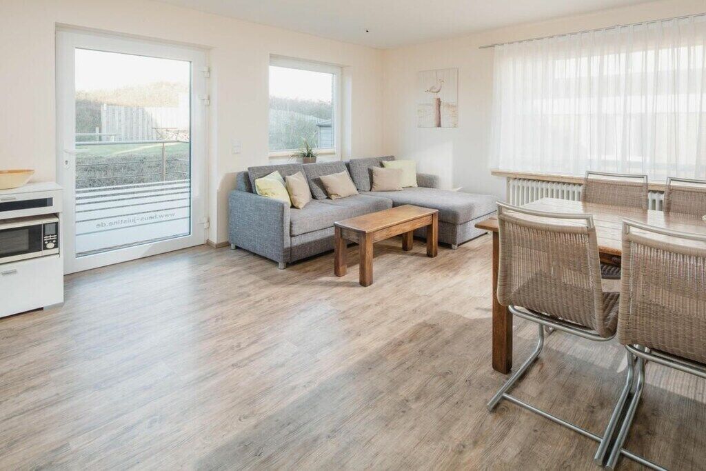 A modern living room with a grey sectional sofa, a wooden coffee table, and a dining area with wicker chairs.